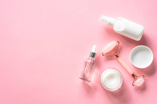 Natural cosmetics on pink. Skin care product, cream, soap serum, jade roller. Flat lay image with copy space. - Fotó, kép