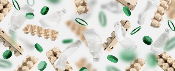 Újrahasznosított kartonból készült tojáskarton, műanyag palackok és palack kupakok zöld háttér lebeg a levegőben.Papír és műanyag újrahasznosítási koncepció. A környezeti fenntarthatóság és a természetbiztonság gondolata - Fotó, kép