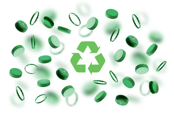 Зеленые крышки бутылки, символ переработки на белом фоне. Пластиковые шапки плавают, летают в воздухе. Концепция безопасности от ущерба окружающей среде. Идея экологической устойчивости, День Земли. - Фото, изображение