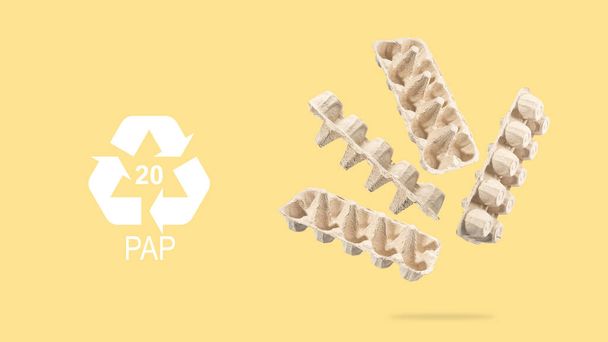 Újrahasznosító szimbólum, újrahasznosított kartonból készült tojásos kartondoboz szürke alapon. Tojástartó legyek és lebegők újrahasznosítására a levegőben. A környezeti fenntarthatóság eszméje.A környezeti károkkal szembeni biztonság - Fotó, kép
