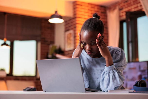 Виснажена молода жінка-фрілансер сидить біля ноутбука, виснаження і навантаження на роботі. Стомлена афроамериканська бізнесменка, яка страждає від головного болю, нещасний працівник на робочому місці. - Фото, зображення