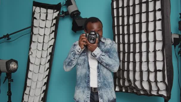 Male photographer using dslr camera and lens to take pictures in studio backstage, capturing photos with professional equipment. Using focused view to photograph images over background. - Filmagem, Vídeo