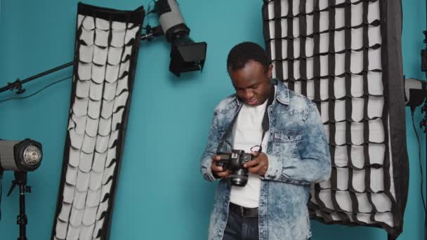 Photographer looking at dslr camera to check image in studio, taking pictures with photography equipment and lighting. Male model using focus lens, backstage lights and tools as hobby. - Materiaali, video