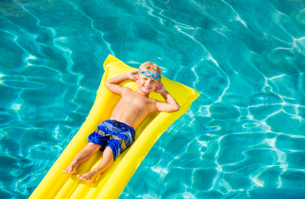 Garçon se détendre et s'amuser dans la piscine sur le radeau jaune
 - Photo, image