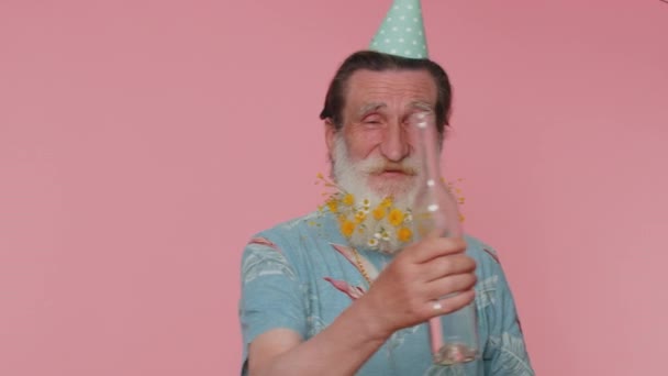 Drunk senior man after party drinks vodka beverage from bottle, celebrating victory win. Alcohol dependence addiction problem, crisis. Elderly grandfather isolated alone on pink studio wall background - Footage, Video