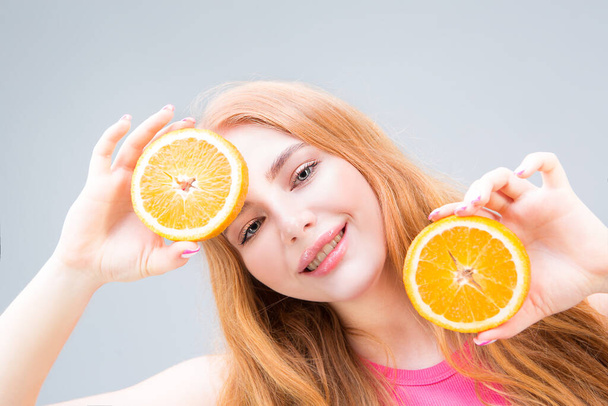 Funny smiling young woman holding juicy halves of oranges isolated on gray background. Healthy eating concept. Diet. - Photo, Image