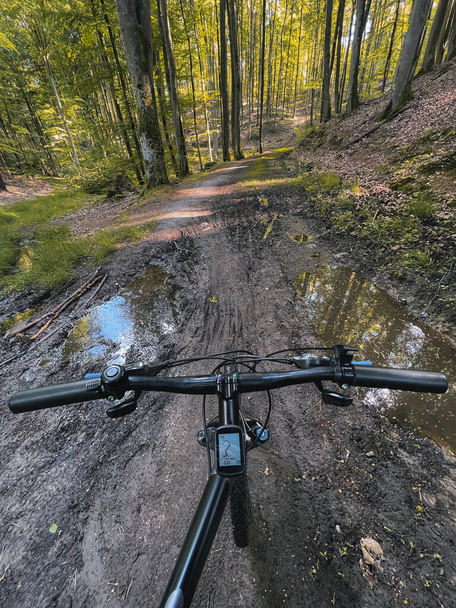 POV photo of riding a bicycle on the forest muddy path. Close up of a bike handlebar with a forest background. Concept of extremely rural and outdoor bike riding. - 写真・画像