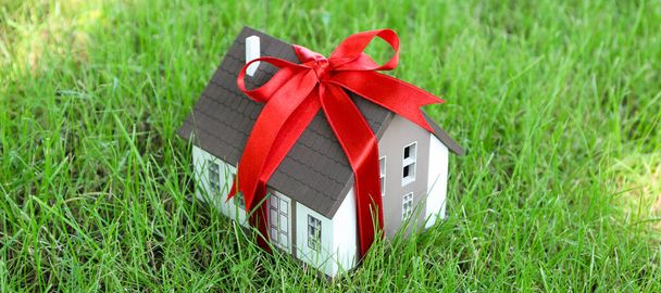 Модель дома с красной лентой на зеленой лужайке - Фото, изображение