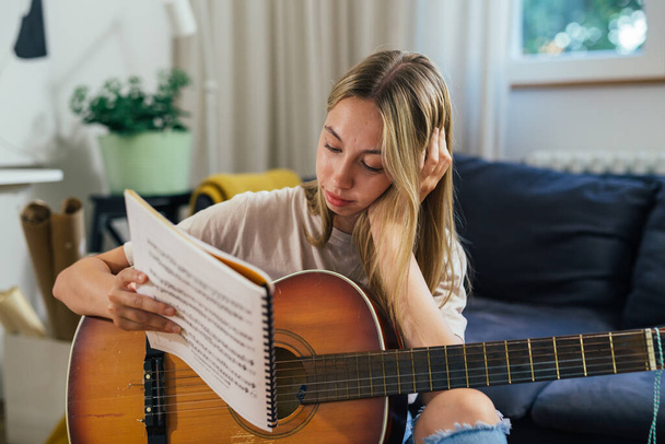teenager reading songbook and playing acoustic guitar at home - Foto, immagini