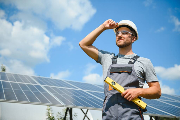 Male worker with solar batteries. Man in a protective helmet. Installing stand-alone solar panel system. - Фото, изображение