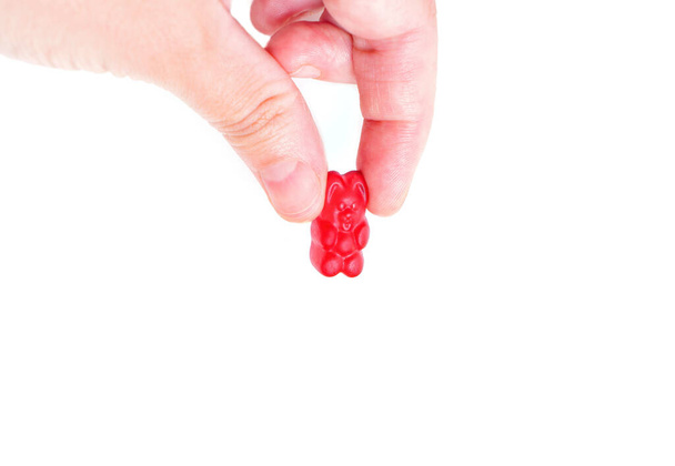 Hand pinch holding and squeezing a red gummy bear candy isolated on white background, close-up. - Foto, imagen