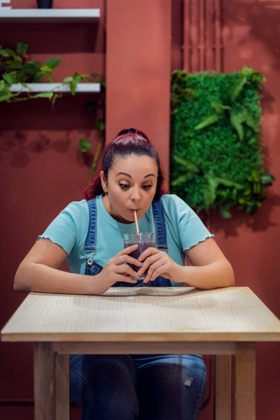 Young woman enjoying drinking a smoothie with a straw in a cafe. Healthy lifestyle and drinks concept. - 写真・画像