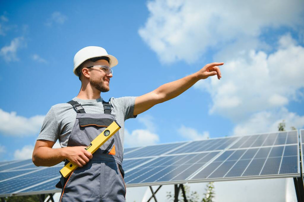 Male worker with solar batteries. Man in a protective helmet. Installing stand-alone solar panel system. - Foto, Bild