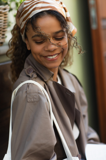 портрет веселой африканской женщины в платке и плаще на улице в Праге  - Фото, изображение