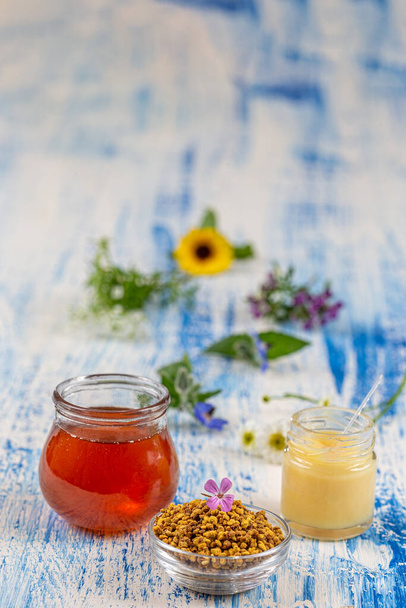Μέλι, γύρη και βασιλικός πολτός με φαρμακευτικά λουλούδια στο παρασκήνιο εναποτίθενται σε μια παλιά σανίδα. - Φωτογραφία, εικόνα