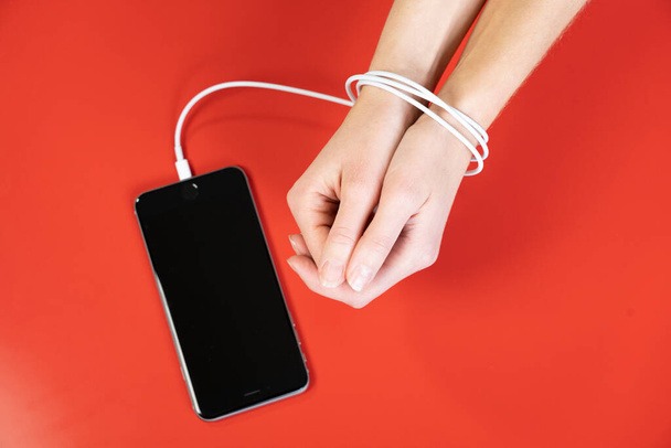 Woman's hands tied by the cord for charging a smartphone. - Фото, изображение