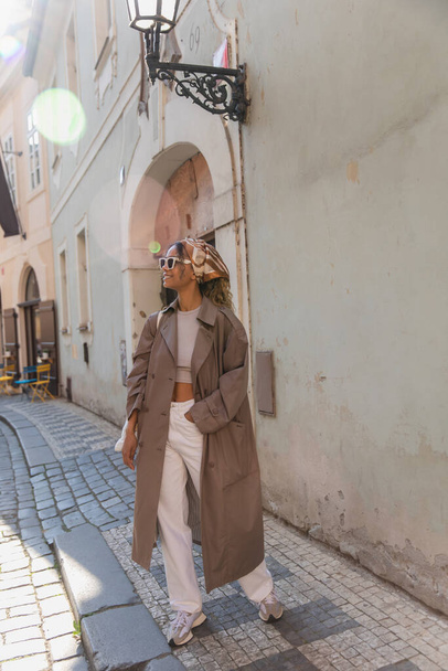 full length of stylish african american woman in trendy accessories posing with hand in pocket on street in prague - Foto, Bild