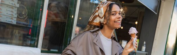 cheerful african american woman in headscarf and stylish trench coat holding ice cream in prague, banner - Фото, зображення