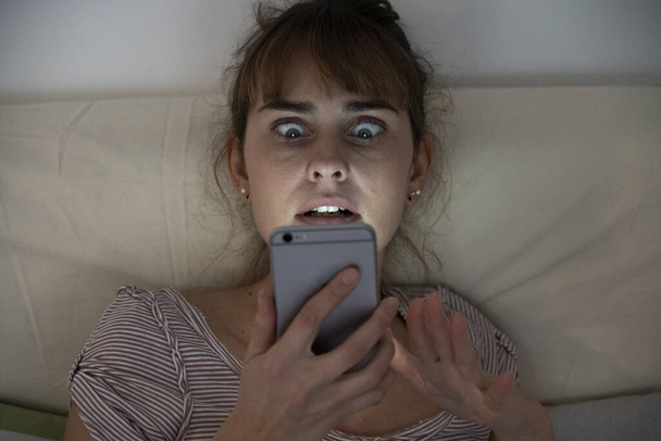 Woman at night admiring her lit smartphone. Addictive behavior. - Photo, image