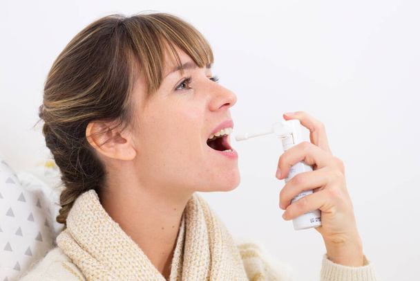 A woman with a sore throat using a mouth spray. - Valokuva, kuva