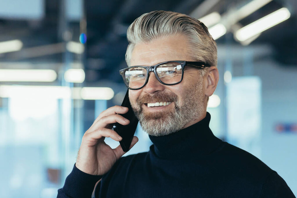 Close-up photo portrait of senior experienced male salesman, businessman in glasses and beard smiling and looking at camera, successful banker investor working in modern office, boss at work - 写真・画像
