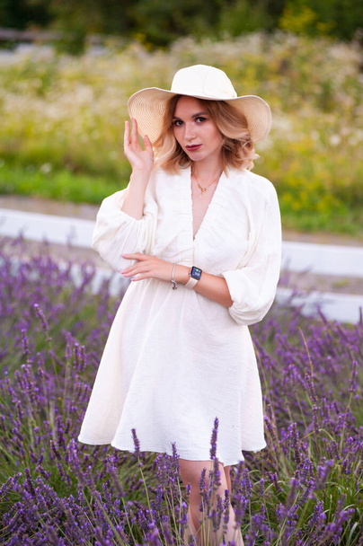 beautiful girl in a white dress and hat in a lavender field at sunset - Foto, Bild