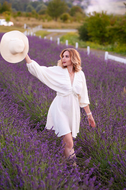 beautiful girl in a white dress and hat in a lavender field at sunset - Foto, immagini