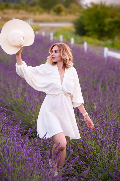 beautiful girl in a white dress and hat in a lavender field at sunset - Foto, afbeelding