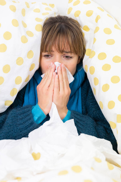 Νεαρή γυναίκα στο κρεβάτι που υποφέρει από κρύωμα με μαντήλια.. - Φωτογραφία, εικόνα