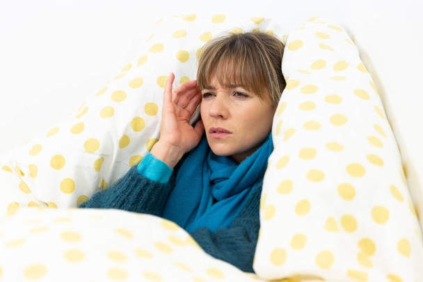 A young woman wrapped up in bed suffering from a flu-like condition with a migraine. - Foto, afbeelding