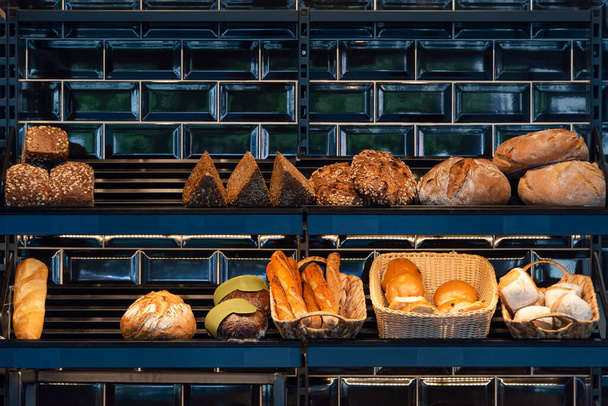 Freshly baked bread on a shelves in bakery, baguette and rolls. Different types of delicious loaves of bread in a german baker shop. - Foto, Imagem