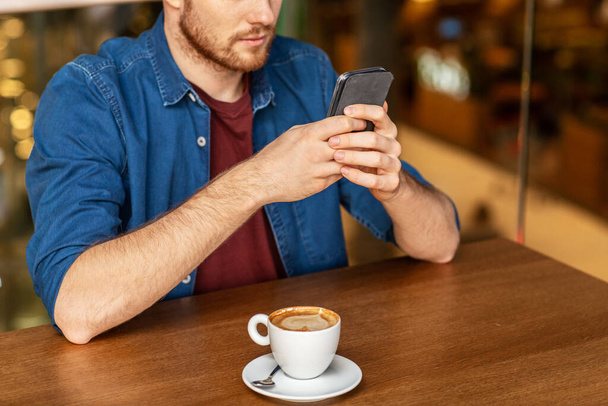 people, technology and leisure concept - close up of man drinking coffee and messaging on smartphone at restaurant or cafe - Zdjęcie, obraz