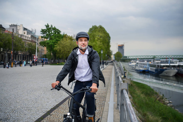 A businessman commuter on the way to work, riding bike next to river, sustainable lifestyle concept. - Фото, изображение