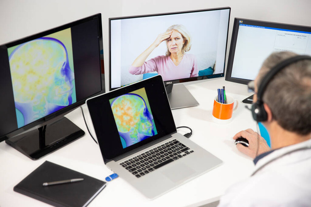 A GP during a video consultation with a 45-year old woman for head pain. An x-ray of her brain can be seen on the screen. - Photo, Image