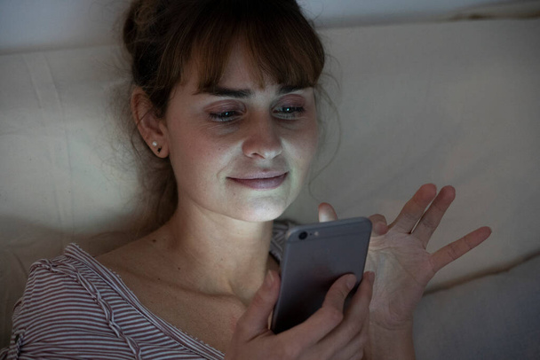 Woman at night admiring her lit smartphone. Addictive behavior. - Photo, image
