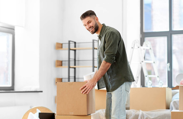 moving, people and real estate concept - happy smiling man with boxes with stuff at new home - Фото, зображення