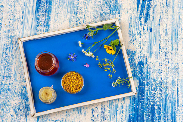 Honey, pollen and royal jelly with medicinal plants deposited on a tray in top view. - Photo, image