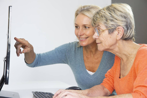 Μια πενηντάρα που βοηθάει μια ηλικιωμένη γυναίκα να χρησιμοποιήσει υπολογιστή.. - Φωτογραφία, εικόνα