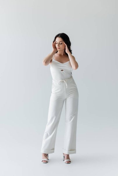 Full length of brunette model in white clothes standing on grey background - Foto, immagini