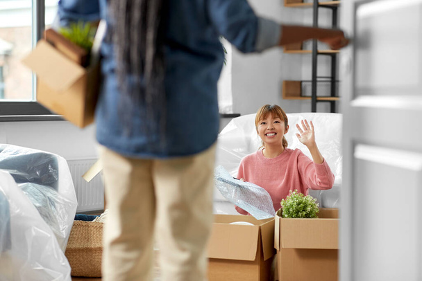moving, people and real estate concept - woman unpacking boxes at new home and her friend entering room - 写真・画像