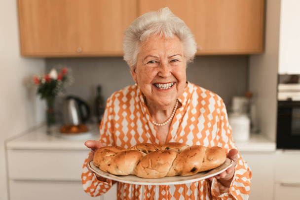 Happy senior woman holding homemade sweet braided bread with raisins. - Zdjęcie, obraz