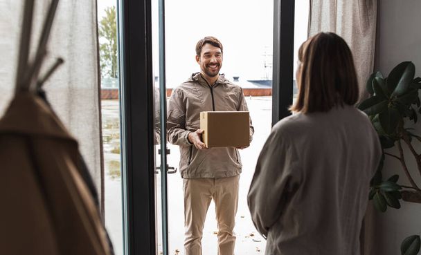 shipping, transportation and people concept - delivery man with parcel box and customer at home - Foto, Imagem