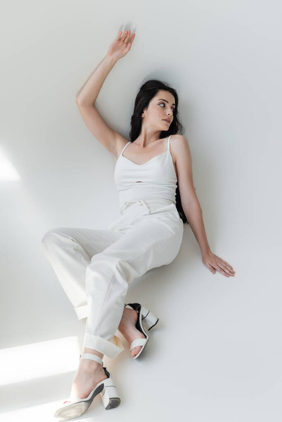 Trendy model in white clothes posing on grey background with sunlight  - Zdjęcie, obraz