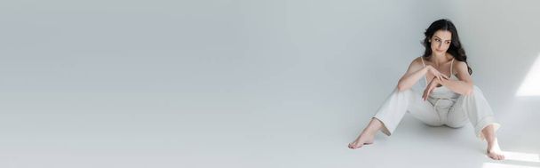 Young model in white clothes looking at sunlight on grey background, banner  - Foto, Imagen