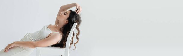 Side view of long haired model posing near chair isolated on grey, banner  - Fotó, kép