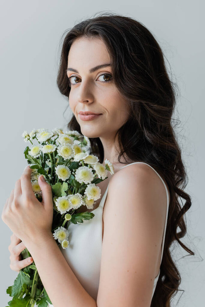 Portrait of long haired model holding flowers isolated on grey  - Foto, afbeelding