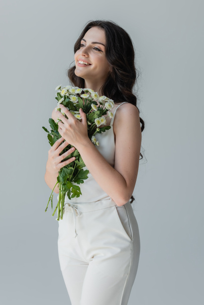 Cheerful woman holding bouquet and looking away isolated on grey  - 写真・画像