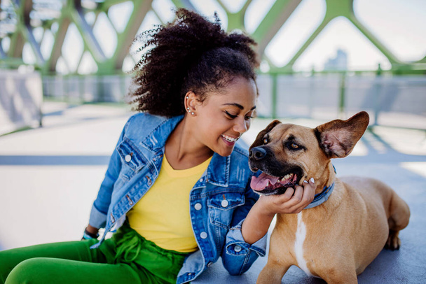 Multiracial girl sitting and resting with her dog outside in the bridge, training him, spending leisure time together. Concept of relationship between a dog and teenager, everyday life with pet. - Foto, Imagen