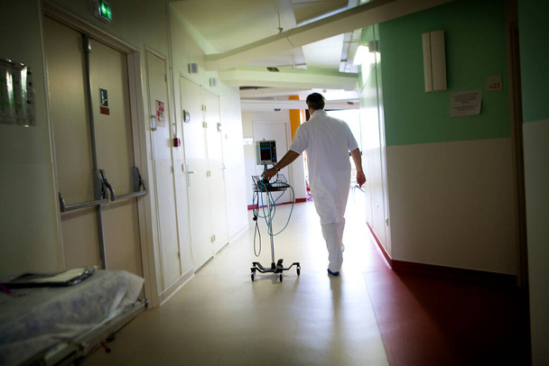 Άνδρας νοσοκόμος με ηλεκτρονικό πιεσόμετρο σε διάδρομο νοσοκομείου. - Φωτογραφία, εικόνα