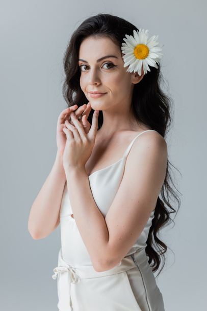 Pretty woman with chamomile in hair looking at camera isolated on grey  - Photo, Image